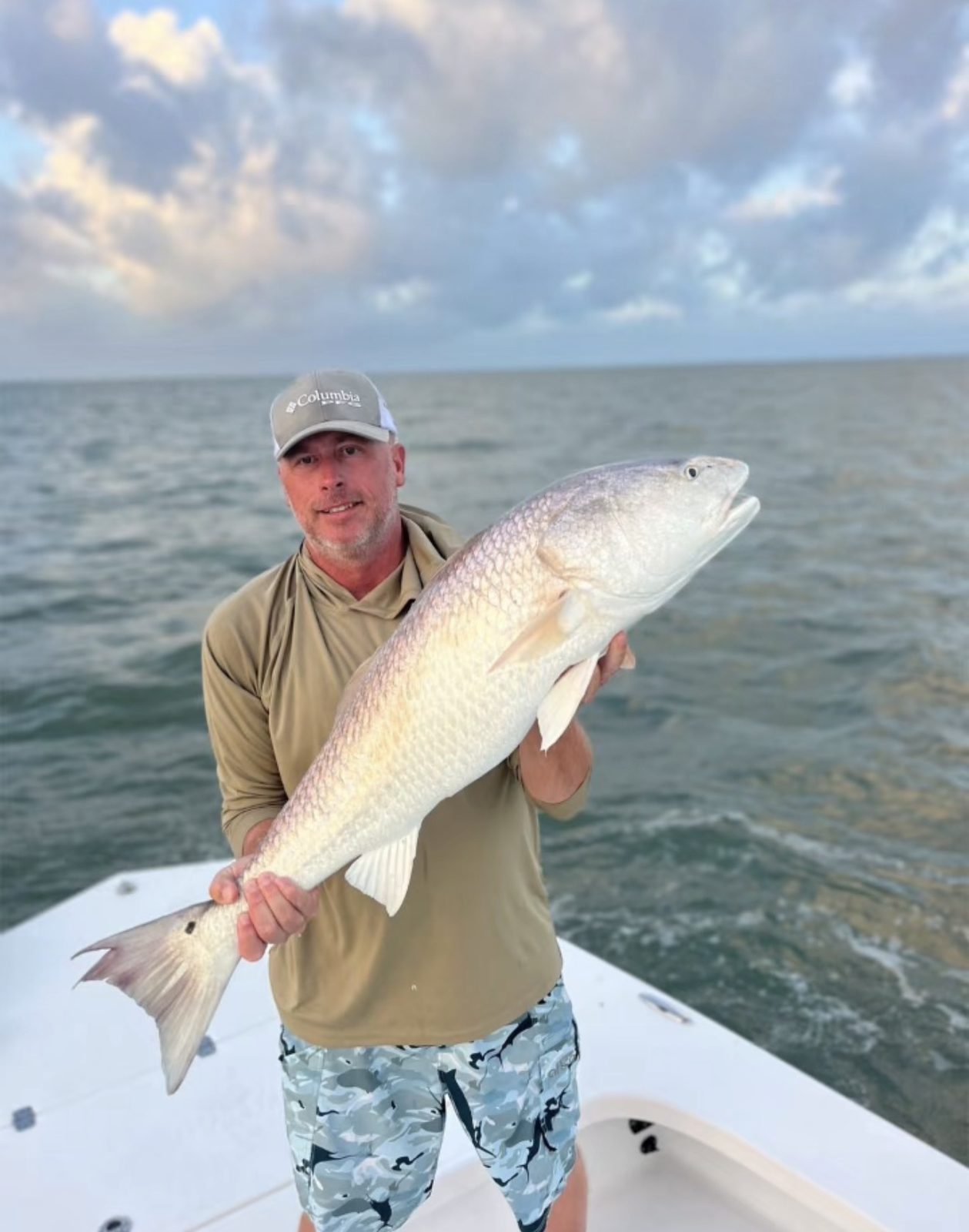 An angler holding a large bull redfish on the bow of the boat at dawn