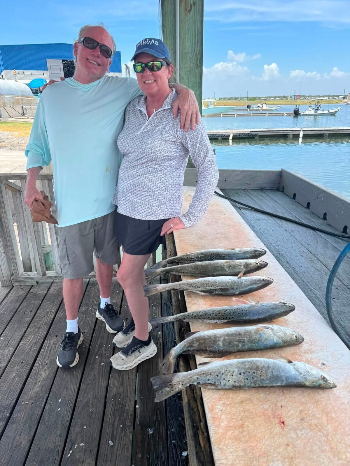 Two anglers at the dock beside a row of speckled trout on the cleaning table